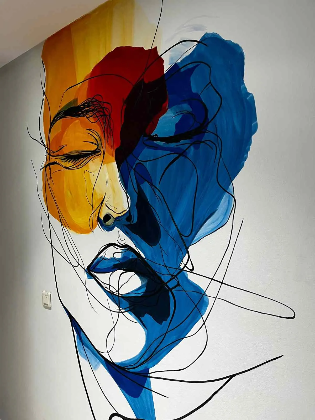 Visage peint au trait noir sur des aplats jaune, rouge et bleu